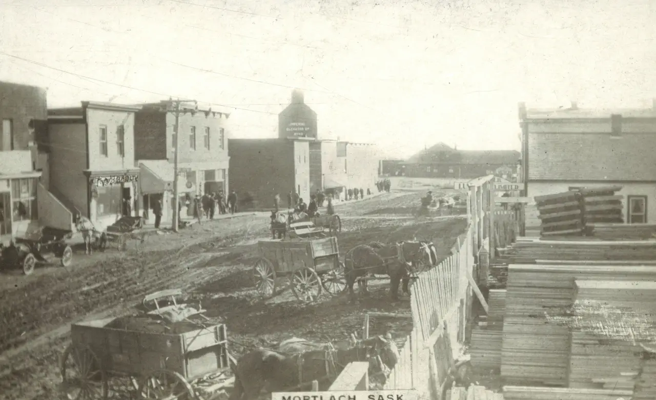 Mortlach street scene with horse-drawn wagons and lumber pile, about 1910